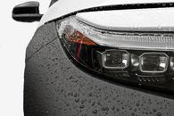 Detailed close-up of a car headlight with raindrops on the surface, showcasing modern design.